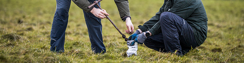 Two people taking samples from the soil and putting it into a bag