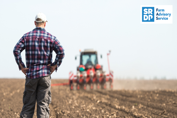 Man standing behind and watching a tractor sowing ssed