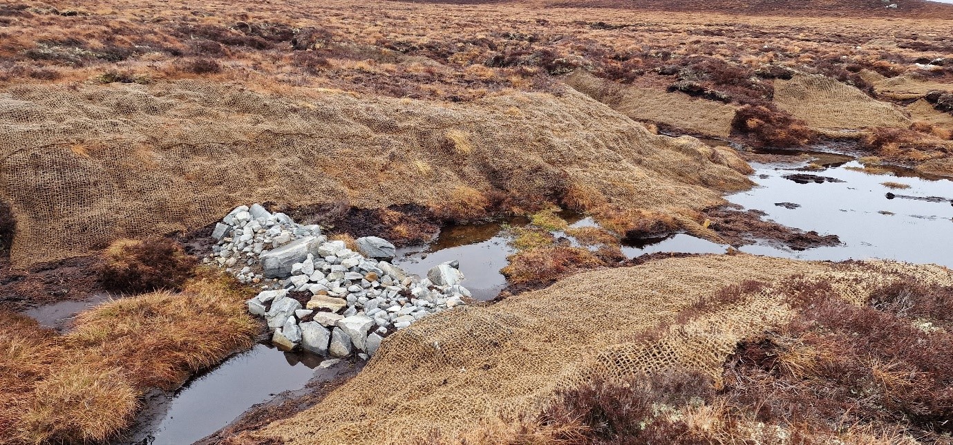 Peatland - Stone Dam A stone dam used in wide channel which was previously eroded down to mineral layer. The eroding sides of the channel have been covered by geotextiles to stop the erosion and encourage vegetation growth.